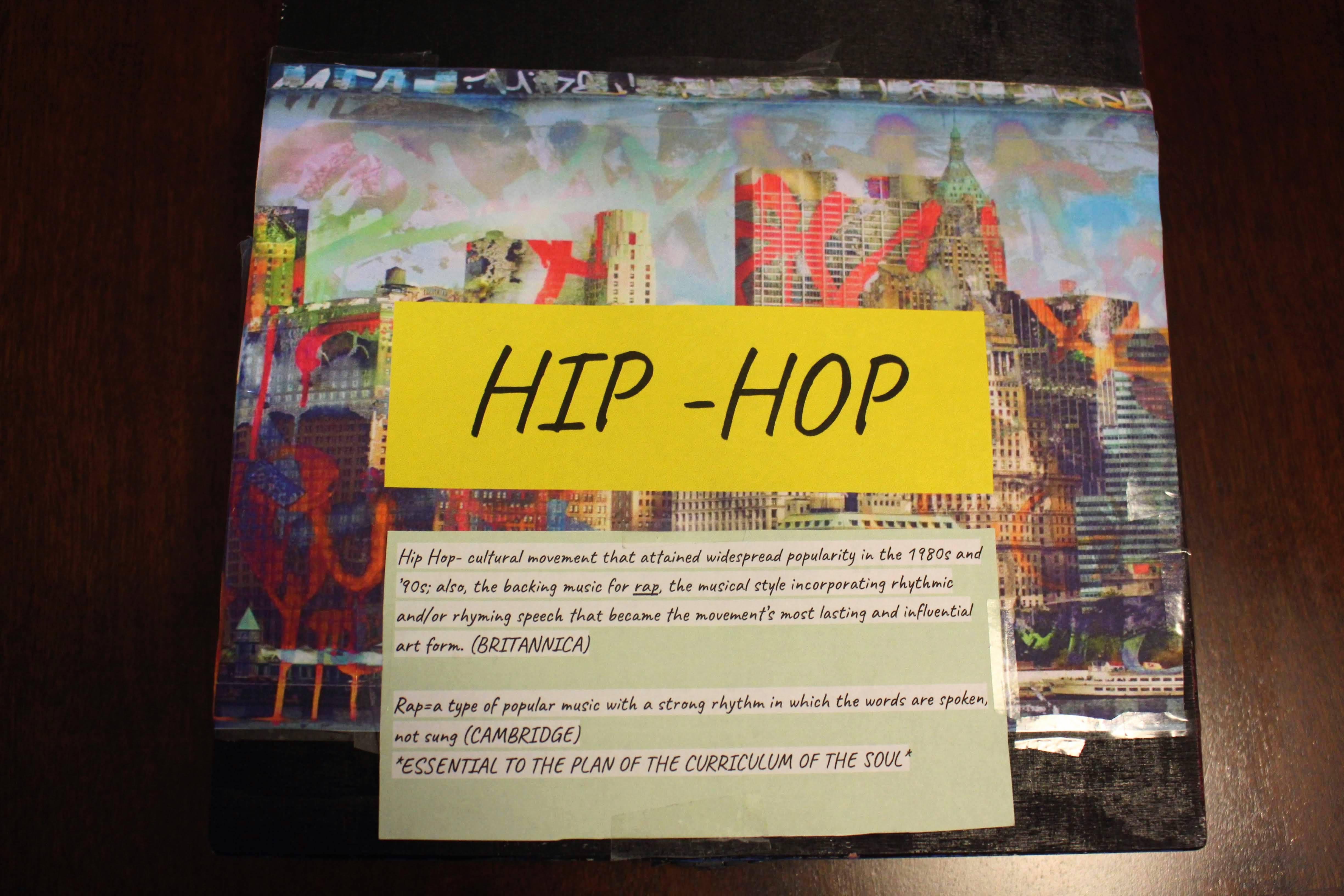 The top of the Hip-Hop keepsake box. Acrylic on wood. On the top of the box is a cutout of Derek Prospero’s “Graffiti City” .Placed on top the wallpaper are definitions for ‘hip-hop’ and ‘rap’ from Brittanica and Cambridge.
